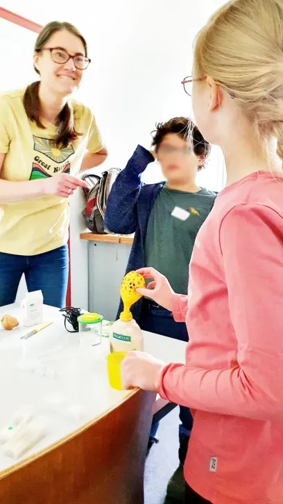 Ein Coach begleitet zwei Kinder beim Hefe-Ballon-Experiment in der MINT Garage